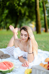 年轻的白种女人躺在公园的格子上看书。