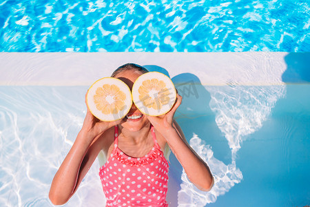 小女孩在背景游泳池的眼睛附近用柠檬半遮住眼睛