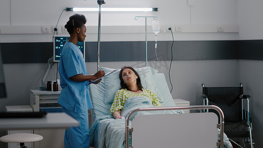 美国黑人助理坐在医院病房的床上检查生病的妇女