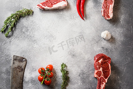 生混合牛肉黑安格斯战斧牛排或斯宾塞牛排，用肉美国切肉刀在灰色石桌石板上切割顶视图框架，配以调味料、西红柿、大蒜、迷迭香。
