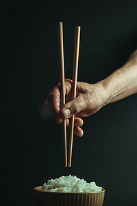 极简主义背景摄影照片_极简主义的老手在一碗米饭上抓着日本筷子，概念是在黑色背景下用电影色调拍摄的