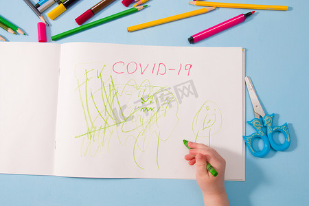 相册热搜摄影照片_一个小孩用铅笔在相册、复制空间、顶视图、蓝色背景、铅笔、蜡笔、剪刀和桌子上的孩子的手上画画