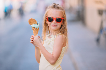 可爱冰淇淋摄影照片_可爱的小女孩在夏天在户外吃冰淇淋。