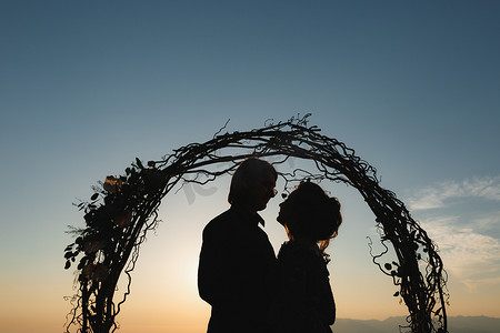 婚礼上日落时在婚礼拱门附近拥抱新娘和新郎的剪影
