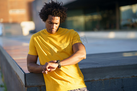 黄色转轮摄影照片_黑人男子查看他的智能手表以查看他的训练数据。