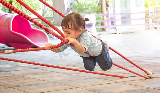 夏天，亚洲小女孩在操场上爬绳子很有趣。