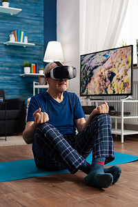 戴着虚拟现实耳机的老人坐在瑜伽垫上练习冥想