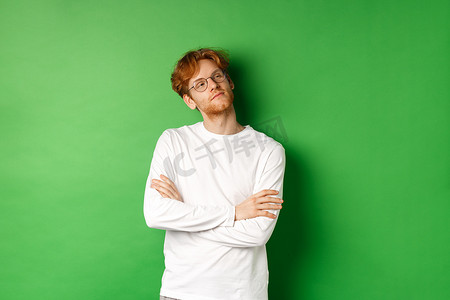 自信的年轻人，一头红发，戴着眼镜，在右侧的复制空间里自鸣得意，胸前自信地交叉双臂，站在绿色背景上
