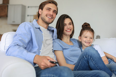 幸福的家庭，孩子坐在沙发上看电视，年轻的父母拥抱女儿一起在沙发上放松。