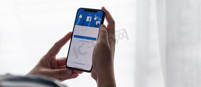 苹果x摄影照片_泰国清迈，2021 年 7 月 18 日：手持 iPhone X 的女性在屏幕上使用社交互联网服务 Facebook。