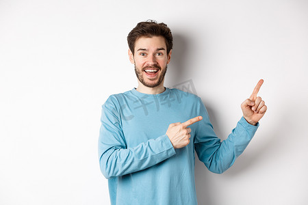 欢快的微笑男子手指向右，在白色空间上展示横幅或标志，用于广告、推荐产品、站在工作室背景上