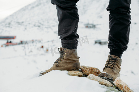 长时间穿着靴子的脚在雪山背景上