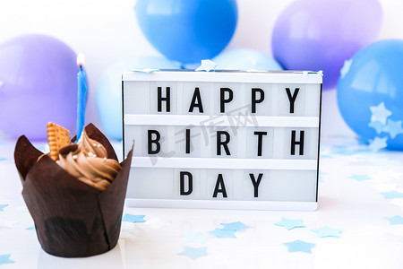 蜡烛模糊背景摄影照片_带有文字“生日快乐”的灯箱和抽象的离焦模糊节日背景上的巧克力蛋糕蜡烛。