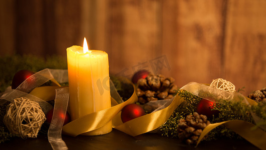 红色大气丝带摄影照片_圣诞概念的温暖：三支蜡烛的特写，在一张深色木桌上点燃，上面有松枝、天然松果、金色和红色明亮的小饰品，上面有金色缎带
