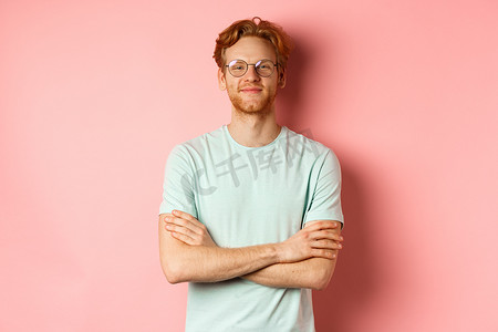 满头红发胡须、双臂交叉在胸前、面带自鸣得意微笑、戴着眼镜、站在粉红色背景上的满意白人男子的画像