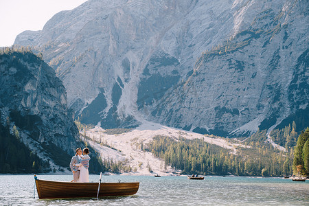 划木船的人摄影照片_新娘和新郎在木船上航行，在意大利的 Lago di Braies 湖上划着桨。