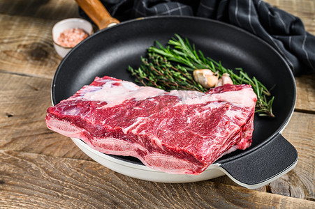 牛仔骨摄影照片_新鲜生牛肉短肋肉放在平底锅上，配上香草。