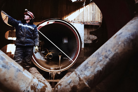 钻井工人摄影照片_工人站在正在施工的管道附近。