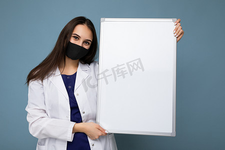 女医生身穿白色医用大衣，戴着面具，拿着空白板，上面有文本隔离的复制空间。
