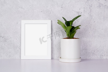 模型白色框架垂直和盆栽在家里的桌面上，模拟海报在办公桌上展示，您的画廊照片和图片设计，边框模板和广告装饰。