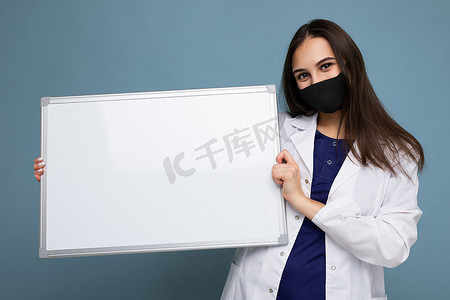女医生穿着白色医用外套，戴着面具，拿着空白板，上面有背景上隔离的文本复制空间。
