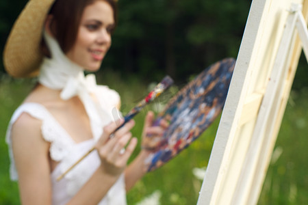 帽子艺术家的漂亮女人在自然油漆上画一幅画
