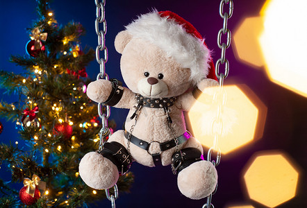 圣诞老人帽子里的泰迪熊是圣诞树背景下 BDSM 游戏的圣诞礼物