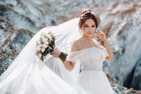 捧花的女孩摄影照片_美丽的新娘穿着婚纱，在盐山顶上捧着一束花。
