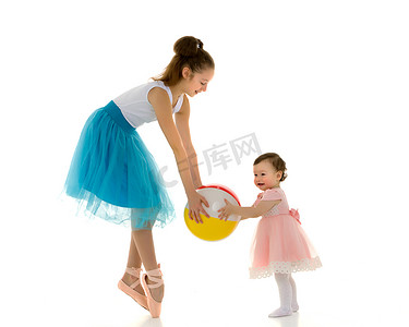 优雅的芭蕾舞演员与可爱微笑的蹒跚学步的小女孩一起玩球。