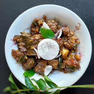 美味的印度风格辣辣椒羊肉精美地放在白碗里，上面镀有洋葱和咖喱叶，对骨头有益