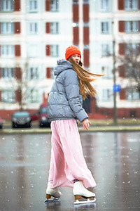 女孩少年在城市的冰上溜冰。穿着长裙和保暖夹克的年轻女孩在冰上。