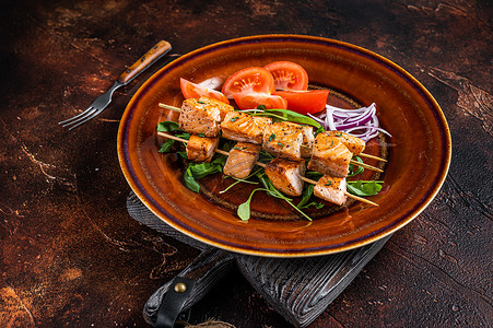 盘子里烤串摄影照片_烧烤三文鱼烤肉串在质朴的盘子里配蔬菜。