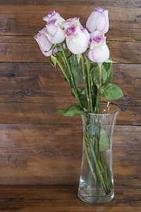浅色木板上的玻璃花瓶中的粉红玫瑰花束，花卉背景。