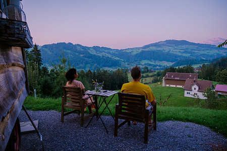 瑞士乡村，Ebnat Kappel，瑞士圣加仑，一对男人和一个女人在瑞士草地上的小屋外看日落