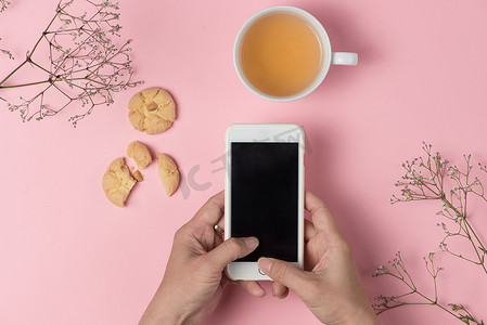 苹果手机样机白色摄影照片_男人手拿着手机喝茶吃燕麦饼干。