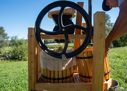 苹果酒摄影照片_用带飞轮的传统压榨机制作苹果酒的人