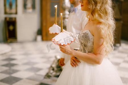 婚纱教堂摄影照片_婚礼期间，新娘和新郎手持蜡烛站在科托尔圣尼古拉斯教堂的祭坛上
