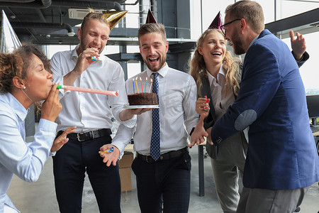 商业聚会摄影照片_带着生日蛋糕的快乐商业团队在办公室聚会上向同事致意