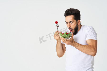 一个穿着白色T恤的男人，盘子里放着沙拉和零食健康食品