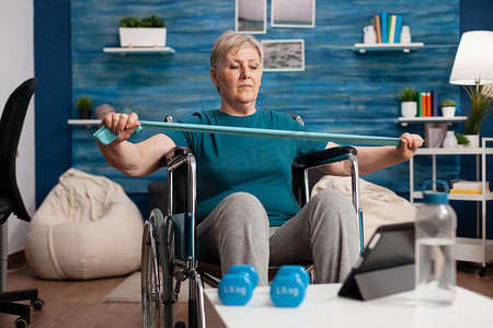 无效老年妇女使用弹力带锻炼手臂肌肉阻力观看健身视频