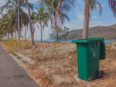 公共服务卫生摄影照片_在靠近大海和棕榈树的现代舒适村庄打开大空绿色塑料垃圾桶。