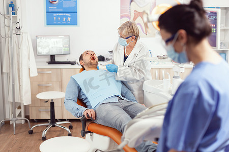 口腔科医生高级医生正在检查病人的口腔，准备进行口腔检查。