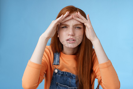 如果没有摄影照片_迷惑不解的可爱风趣的红头发欧洲女人正在寻找眯着眼睛的人，如果没有眼镜，就无法看到远处，手握着前额遮住视线，站在蓝色背景中