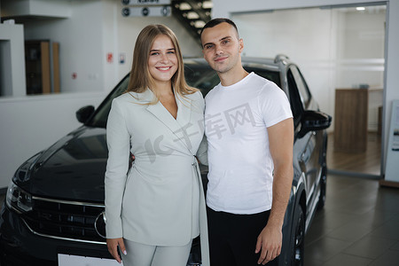从汽车陈列室购买新车后，美丽的年轻夫妇开心的画像。