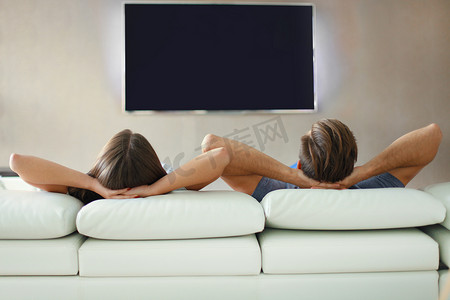 一对夫妇在沙发上放松并在家看电视的后视图