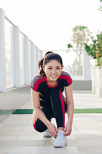 年轻美丽迷人的运动跑步者女人系上她的运动鞋鞋带，微笑着开心地准备在公园跑步和慢跑锻炼。