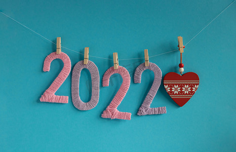 2022 年的针织人物，由粉色和淡紫色的线制成，挂在蓝色背景的衣夹上，上面有一颗红色的心。
