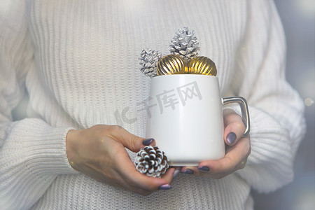 女人手上的白色圣诞杯，上面放着松果 — 冬天的杯子是新年概念的特写