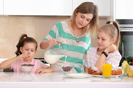 家庭餐摄影照片_母亲在厨房的餐桌上为两个女儿提供早餐，快乐的单身母亲概念