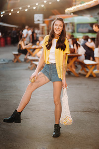 一个穿着黄色衬衫、短裤和黑色鞋子、带着柠檬和柠檬汁的女孩正在城市街道上行走。